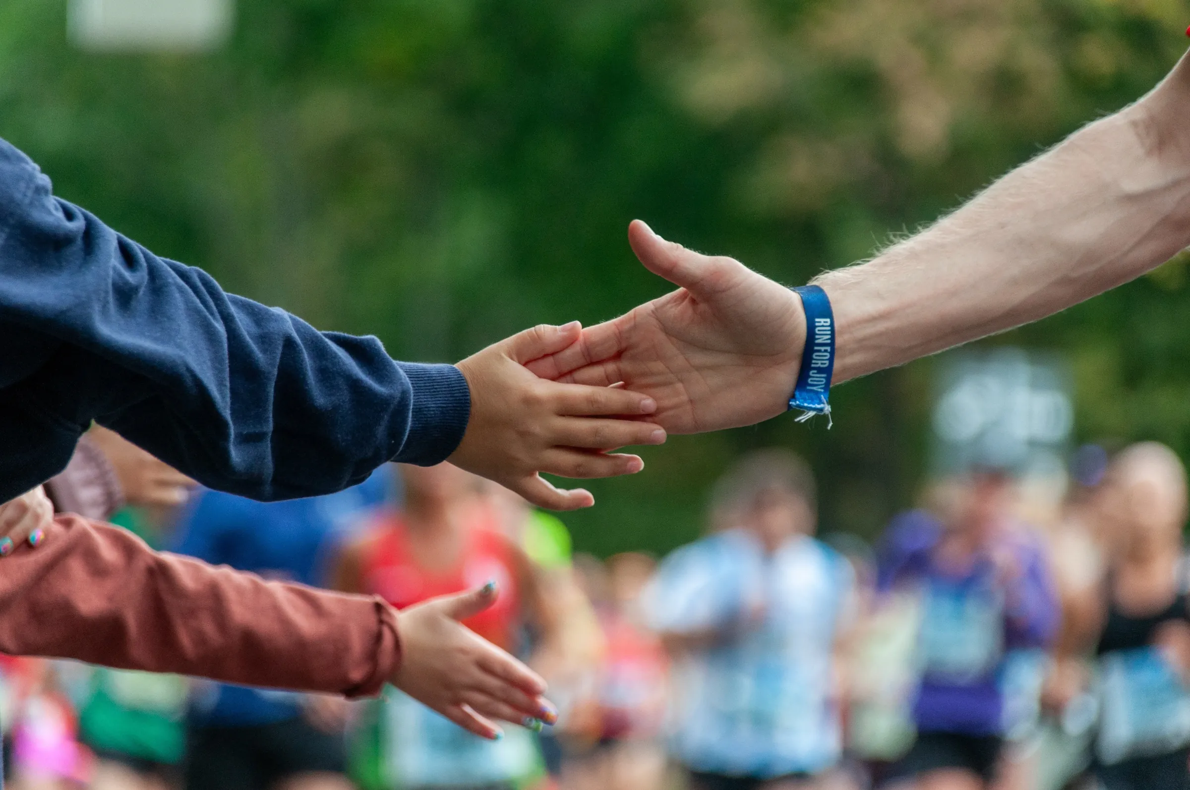 Outstretched hands reaching to meet in a high-five, with a blurred crowd of participants behind them.