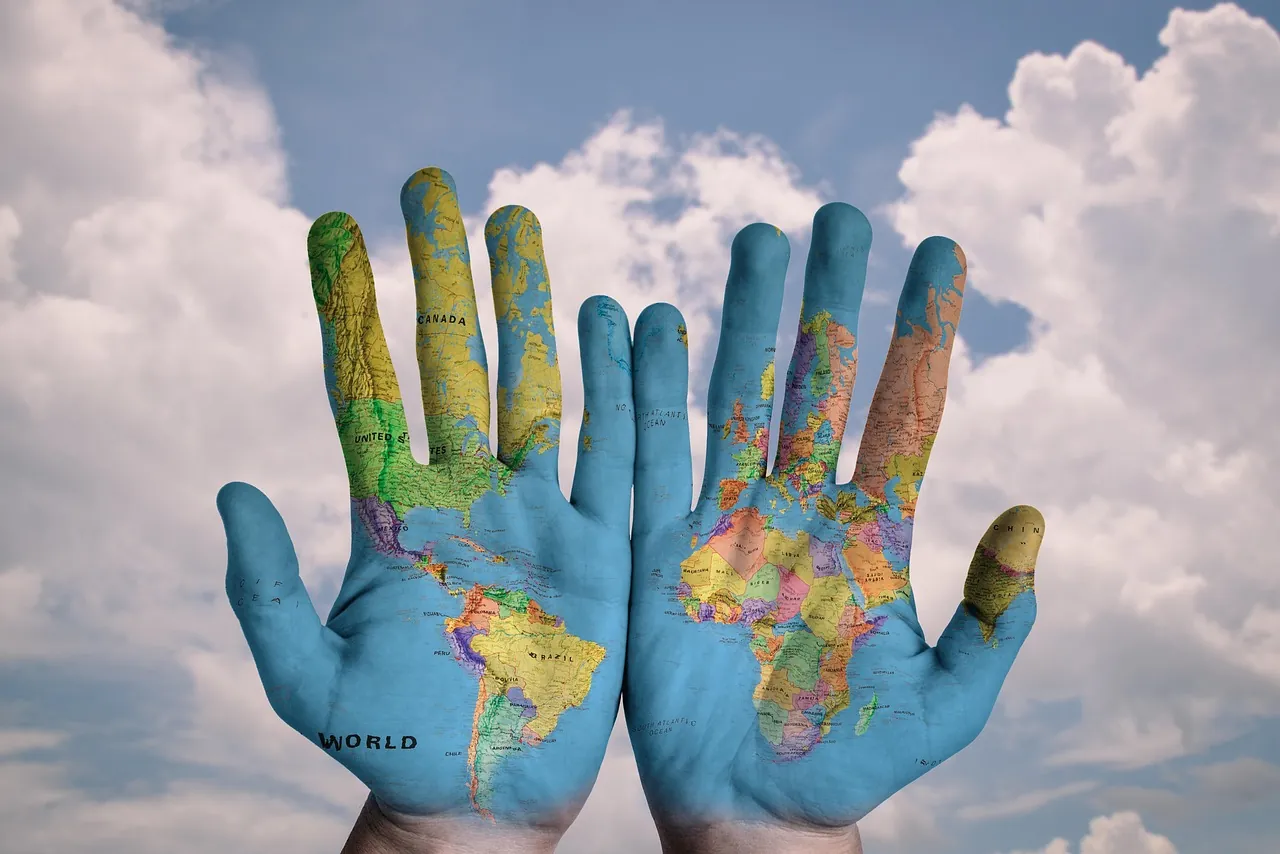 Two open hands raised to the sky, their palms painted with a colourful map of the world.